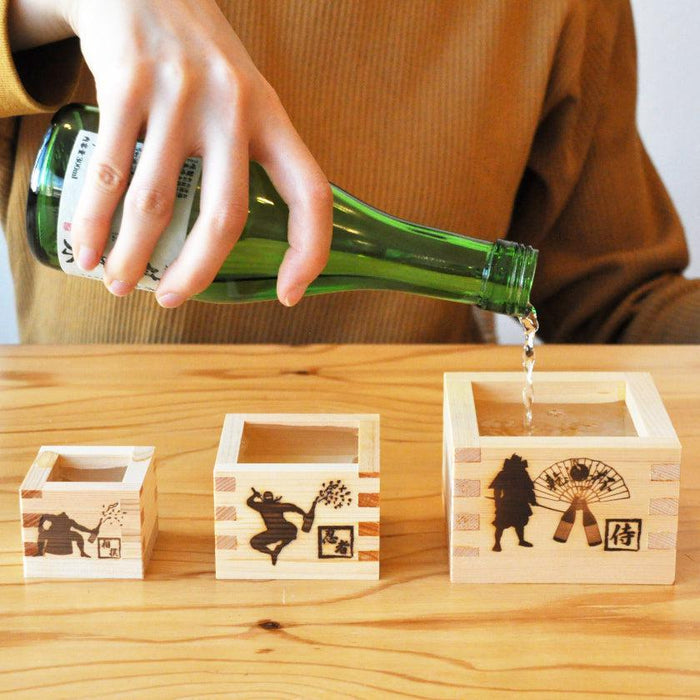 Wooden masu sake cups set of three with samurai and ninja designs, sake being poured | J.Flavor × Ohashi, Japan