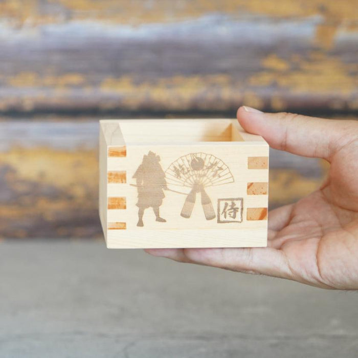Wooden masu sake cup with engraved samurai and fan design held in hand | J.Flavor × OHASHI, Japan