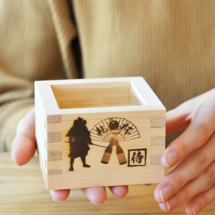 Wooden masu sake cup with samurai silhouette engraving, held in both hands | J.Flavor × OHASHI, Japan