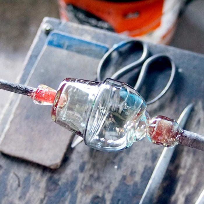 Ryukyu glass cup being shaped on metal rods during glassblowing process, Okinawa workshop