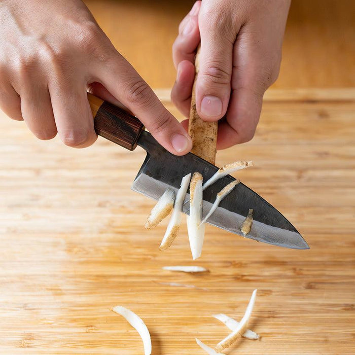 Shinbu Deba knife 120mm slicing burdock root on a wooden cutting board | Fukube Kaji, Ishikawa