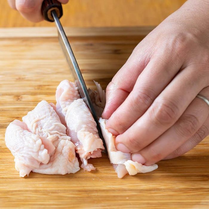 Hands slicing raw chicken on a wooden cutting board with a Japanese kitchen knife | Fukube Kaji, Ishikawa