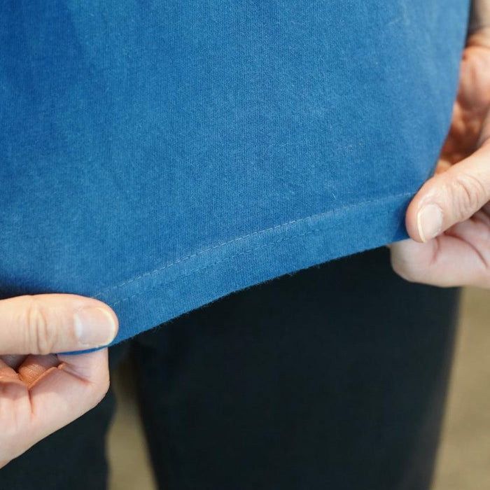 Close-up of hem stitching on a natural indigo-dyed t-shirt being held up | Indigo Kesennuma